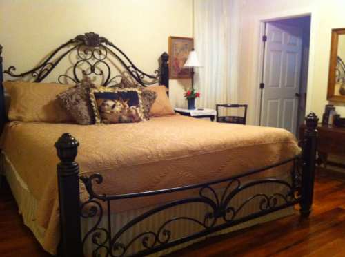 A cozy bedroom featuring a large wrought iron bed with decorative pillows, a bedside lamp, and wooden furniture.
