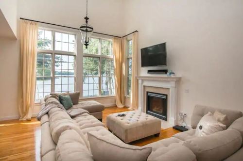 Bright living room with large windows, a cozy sectional sofa, a fireplace, and a TV, overlooking a scenic view.