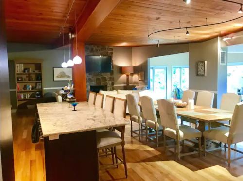 A spacious kitchen and dining area with a large table, bar seating, wooden beams, and a stone fireplace.