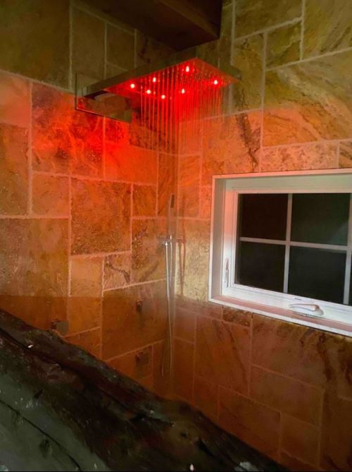 A modern shower with a rain showerhead and red LED lights, set against a stone wall and a window.
