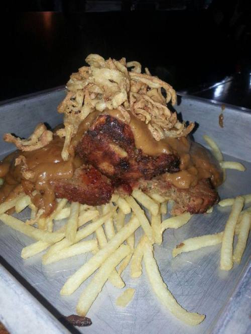 A plate of fries topped with a large portion of meat covered in gravy and crispy fried onions.