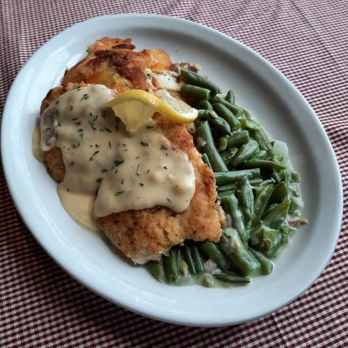 A plate of fried fish topped with creamy sauce and a lemon slice, served with green beans on the side.
