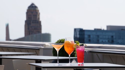 Three colorful cocktails on a rooftop table with a city skyline in the background.