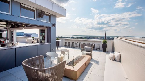 Rooftop terrace with modern seating, a fire pit, and a view of the skyline under a partly cloudy sky.
