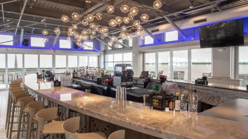 A modern bar with a sleek countertop, stylish stools, and unique lighting fixtures, featuring a well-stocked liquor display.
