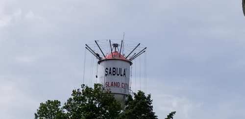 Water tower with "SABULA ISLAND CITY" painted on it, surrounded by trees under a cloudy sky.