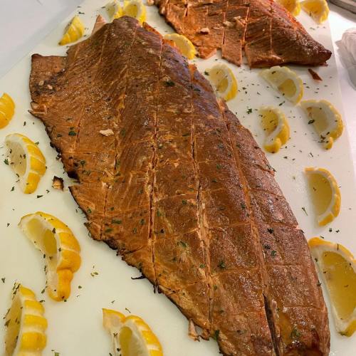 Two beautifully cooked fish fillets garnished with lemon wedges on a white cutting board.