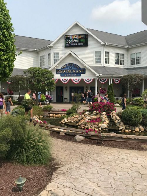 Exterior view of a restaurant with a sign, surrounded by flowers and a pond, featuring festive decorations.