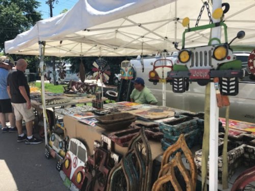 A vendor's booth at a market displaying colorful handmade crafts and decorations, with people browsing nearby.