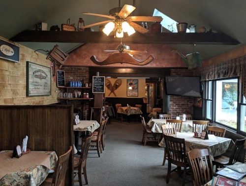 Cozy restaurant interior with wooden tables, ceiling fan, and rustic decor, featuring a warm, inviting atmosphere.