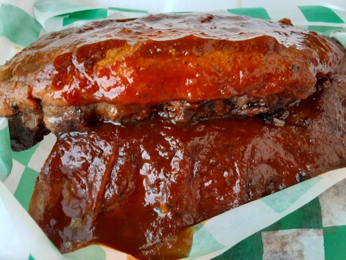 A close-up of a glazed barbecue rib with a rich, thick sauce on a green and white checkered paper.