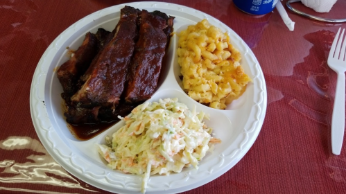 A plate with barbecue ribs, macaroni and cheese, and coleslaw on a white disposable plate.
