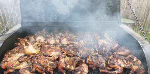 A large grill filled with smoky, grilled chicken pieces, showcasing a delicious barbecue scene.