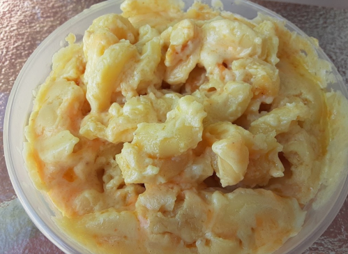 Creamy macaroni and cheese in a clear plastic container, with a rich, cheesy texture and golden color.