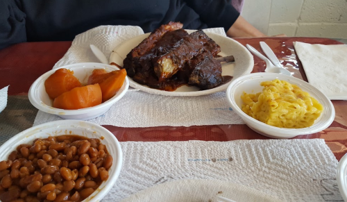 A plate with barbecue ribs, baked beans, macaroni and cheese, and sliced peaches on a table with napkins.