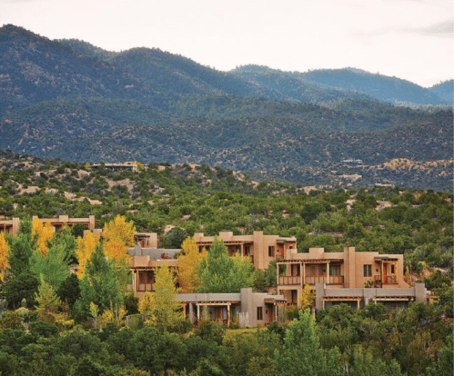 A scenic view of modern buildings nestled among trees and mountains, showcasing autumn colors in the landscape.