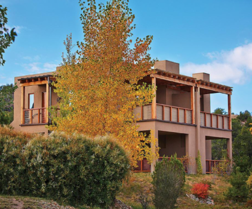 A modern two-story house surrounded by greenery and autumn trees under a clear blue sky.