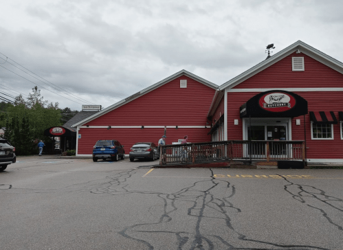 A red building with a sign for a butcher shop, featuring parked cars and people walking outside on a cloudy day.