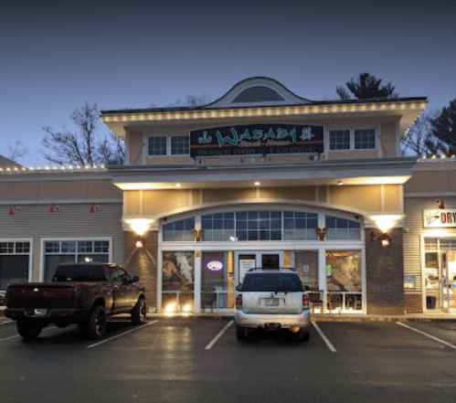 Exterior of Wasabi restaurant at dusk, featuring a sign, large windows, and parked cars in front.