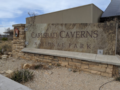 Sign for Carlsbad Caverns National Park, featuring stone and metal design, surrounded by desert landscape.