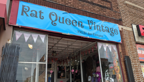 Storefront of "Rat Queen Vintage" with a blue sign and decorative bunting, showcasing vintage items inside.