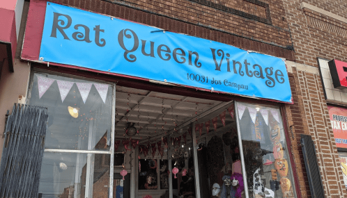 Storefront of "Rat Queen Vintage" with a blue sign and decorative bunting, showcasing vintage items inside.