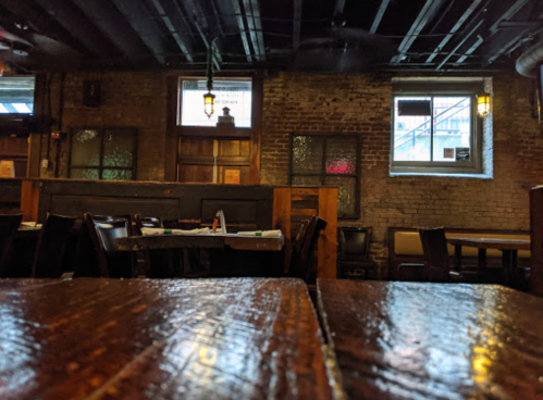 Interior of a rustic restaurant with wooden tables, exposed brick walls, and windows letting in natural light.