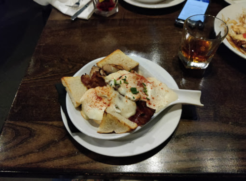 A plate of toast topped with meat, creamy sauce, and spices, served with a drink on a wooden table.