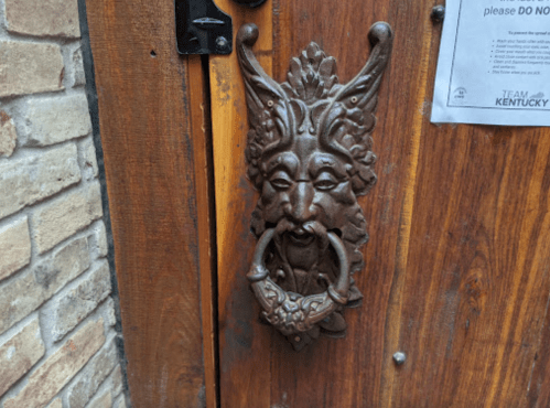 A decorative door knocker shaped like a face with horns, mounted on a wooden door.