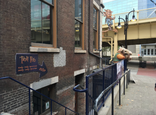 A whimsical entrance to the Troll Pub, featuring a colorful troll figure and a sign pointing to the pub's location.