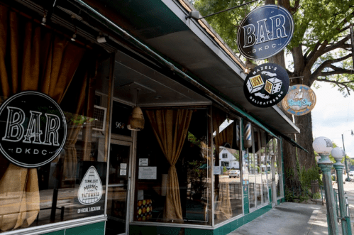 Exterior of a bar and delicatessen with large signs, featuring a green facade and large windows.