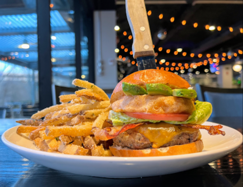 A juicy burger with bacon, cheese, lettuce, and tomato, topped with a knife, served with crispy fries on the side.