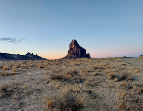 A rocky formation rises from a barren landscape at dusk, with soft pastel colors in the sky.