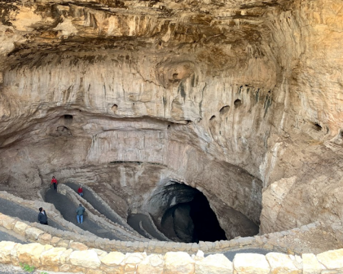A deep cave with textured walls and a winding path, featuring small figures of people at the bottom.