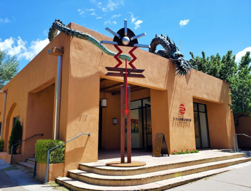 A modern art building with a dragon sculpture on the roof and a colorful totem in front, set against a blue sky.