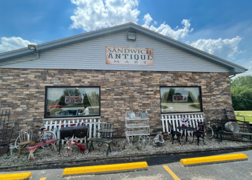 Exterior of Sandwich Antique Mart with stone facade, "OPEN" sign, and vintage items displayed outside.