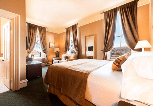 Cozy hotel room with a large bed, armchair, and windows draped in elegant curtains, featuring warm, inviting colors.