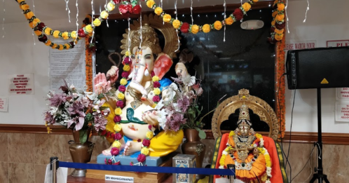 A colorful statue of Lord Ganesha adorned with flowers and decorations, alongside another deity statue in a temple setting.