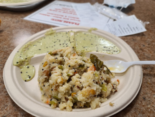 A plate with a serving of textured rice dish and green sauce, set on a brown table with papers in the background.