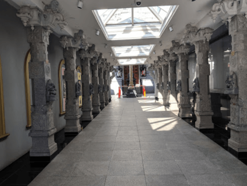 A corridor with ornate stone columns, bright skylights, and polished floors, leading to a distant entrance.