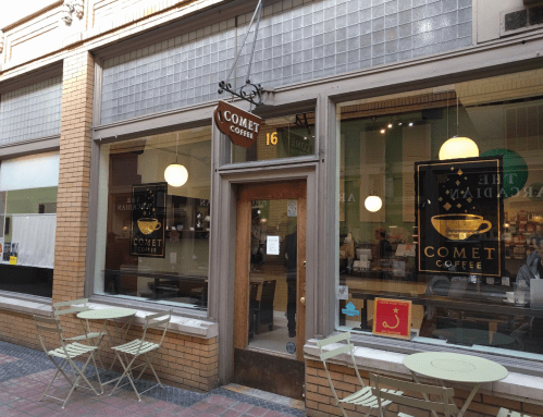 Exterior of Comet Coffee shop with a sign, large windows, and outdoor seating in a brick building.