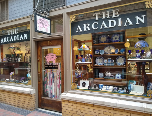 A storefront with large windows displaying various decorative items and a sign reading "The Arcadian."