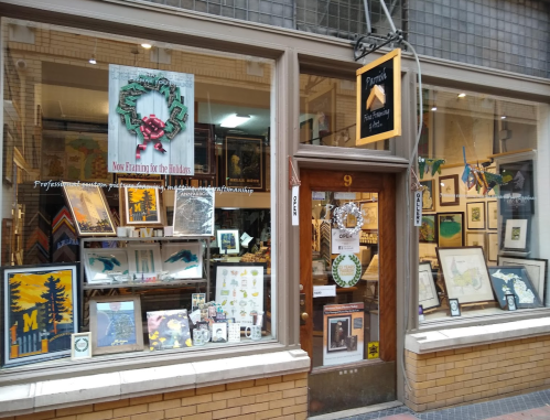 A storefront with a festive holiday display, featuring framed art and decorations in the windows.