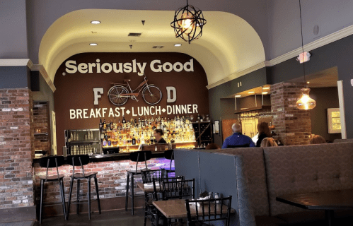 Interior of a restaurant featuring a bar with a bicycle on the wall, and a sign that reads "Seriously Good Food."