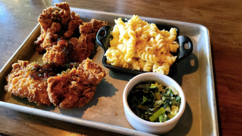 A metal tray with crispy fried chicken, creamy pasta, and a small bowl of greens.