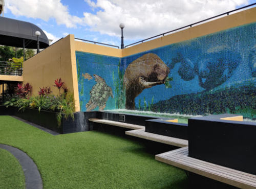 A vibrant mural featuring a turtle and a beaver, surrounded by greenery and seating in a sunny outdoor space.