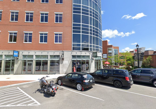 A modern building with large windows, featuring parked cars in front and a clear blue sky above.