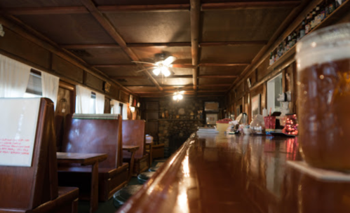 A cozy bar interior with wooden booths, a long counter, and soft lighting, creating a warm atmosphere.