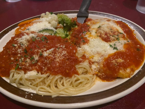A plate of spaghetti with marinara sauce, cheese, and a side of mixed vegetables.