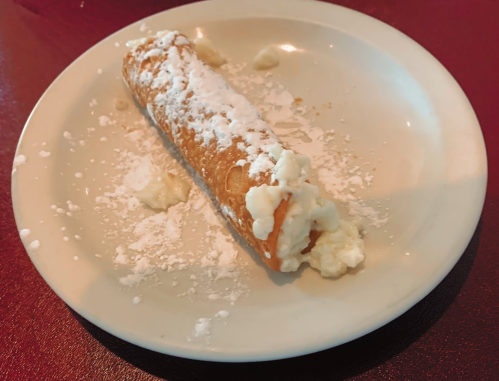 A partially filled cannoli on a white plate, dusted with powdered sugar and creamy filling visible.